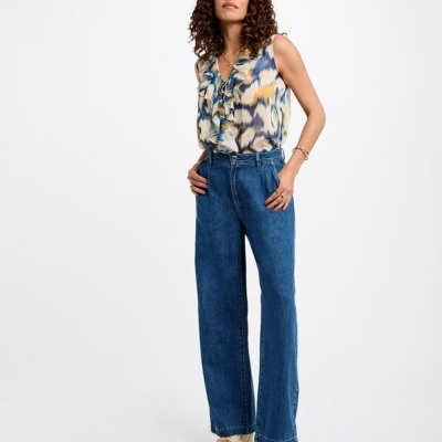 Mulher com blusa colorida e calças de ganga azuis em fundo branco