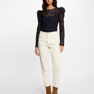 Modelo com blusa preta de renda e calças brancas no fundo branco