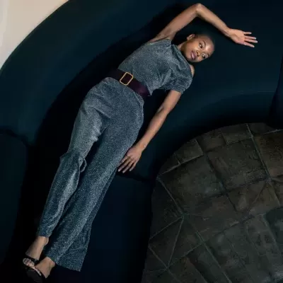 Macacão cinzento brilhante com cinto castanho em mulher num sofá preto curvo