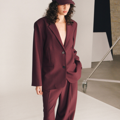 Mulher com blazer e calças bordeaux e boné com texto branco GRACE & MILA