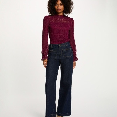 Mulher com blusa roxa de renda, calças jeans azuis largas e sapatos castanhos