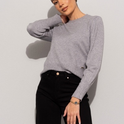 Mulher com camisola cinzenta e calças pretas contra parede branca