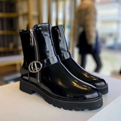 Botas pretas brilhantes com fivela metálica e fecho lateral sobre mesa branca