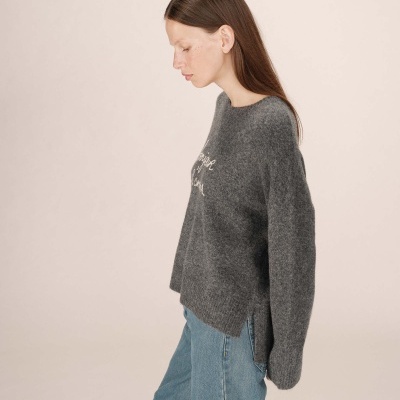 Mulher de perfil com camisola cinzenta e calças de ganga azuis largas