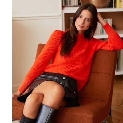 Mulher com camisola laranja e saia preta sentada numa cadeira castanha