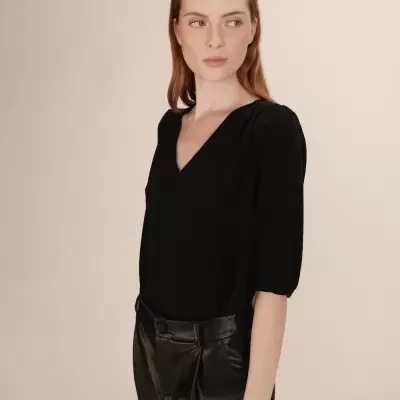 Mulher com blusa preta de decote em V e calças pretas brilhantes