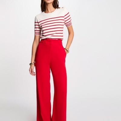 Mulher veste camisola branca às riscas vermelhas e calças vermelhas largas em fundo branco.