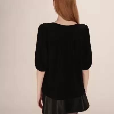 Mulher de costas com blusa preta e calções pretos em fundo neutro