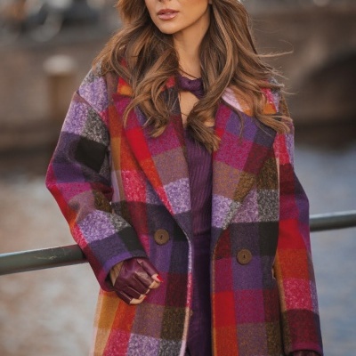 Casaco xadrez vermelho, roxo, laranja com botões, mulher com luvas vinho e gorro felpudo bege.