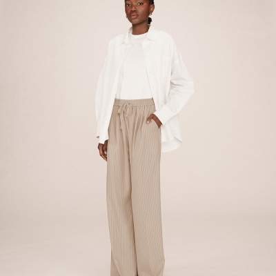 Mulher com calças largas bege riscas finas, camisa branca e camisa branca sobreposta