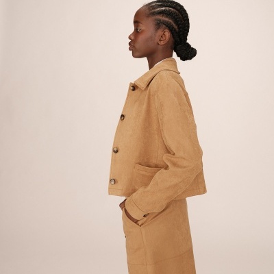 Mulher de perfil com casaco e saia cor camel em fundo neutro