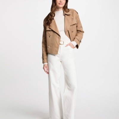 Mulher com casaco bege, camisola branca, calças brancas largas e botas castanhas em fundo branco