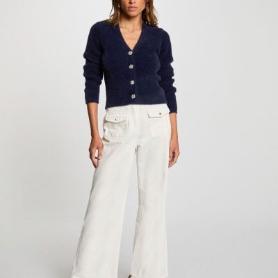 Mulher vestindo camisola azul escura de malha, calças brancas largas e sapatilhas azul e branco