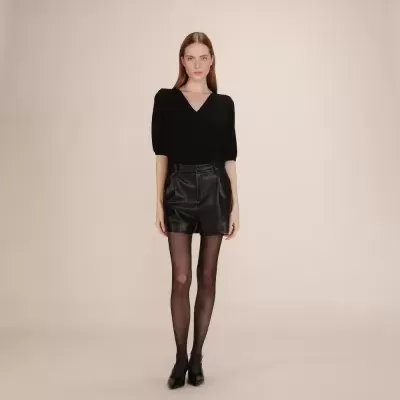 Modelo feminina com blusa preta, calções de pele pretos, collants pretos e sapatos pretos em fundo neutro.