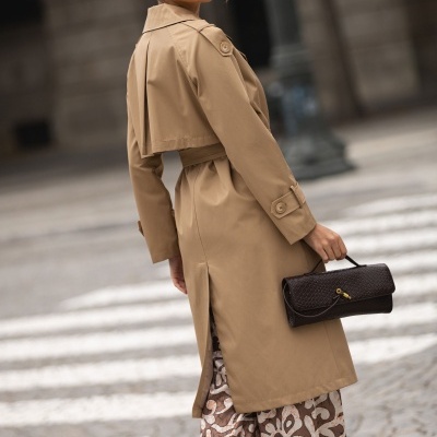 Mulher com gabardina bege e carteira preta numa rua urbana