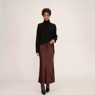 Mulher com camisola de gola alta preta e saia castanha acetinada comprida