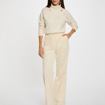 Mulher com camisola de gola alta creme e calças largas creme com botins castanhos