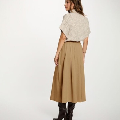 Mulher de costas com cárdigan bege, saia midi beige e botas pretas