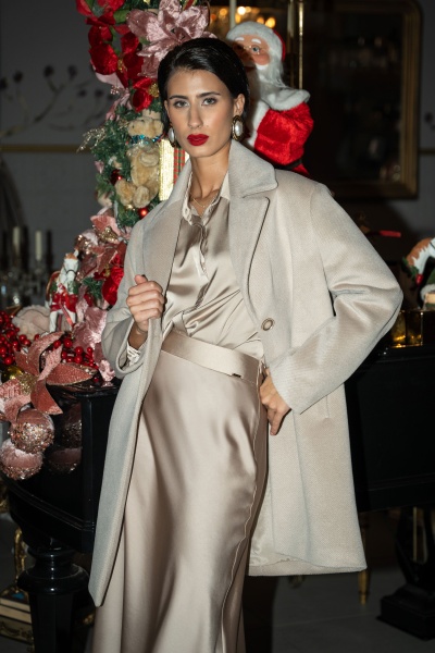 Mulher com casaco bege e roupa acetinada em ambiente com decoração de Natal