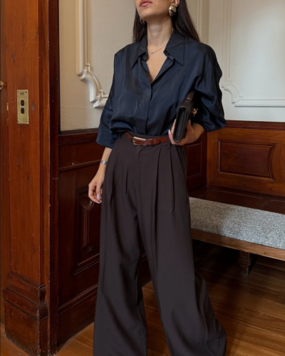 Mulher com camisa preta e calças largas castanho-escuro num ambiente interior