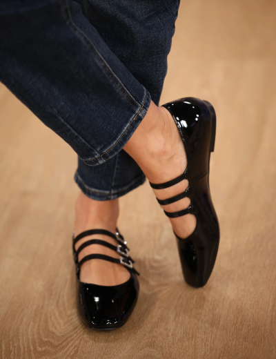 Sapatos pretos de verniz com três tiras e fivelas prateadas em fundo de madeira clara