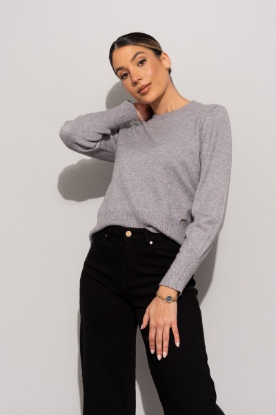 Mulher com camisola cinzenta e calças pretas contra parede branca