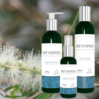 Três frascos de produtos DRY CONFORT verdes com rótulos brancos e detalhes azuis ao lado de flor branca