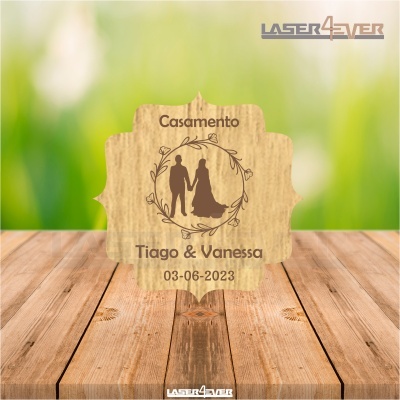 Placa decorativa de casamento em madeira com nomes e data, sobre mesa de madeira.