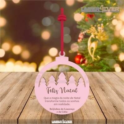 Enfeite de Natal rosa com mensagem pendurado com cordão vermelho em frente a árvore de Natal decorada