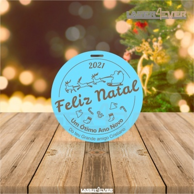 Enfeite redondo azul claro com texto de Natal sobre mesa de madeira e fundo natalício desfocado