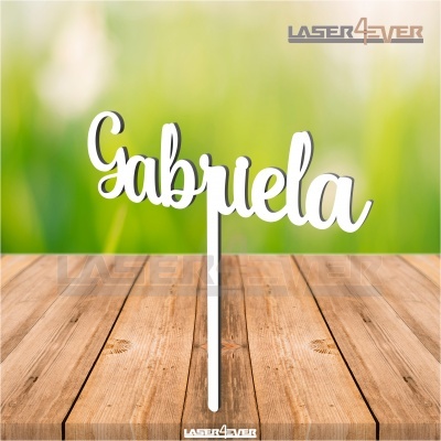 Topo de bolo branco com nome 'Gabriela' em madeira sobre mesa de madeira clara