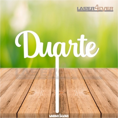 Objeto decorativo branco com palavra Duarte em superfície de madeira e fundo verde