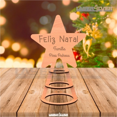 Peça em madeira em forma de estrela com inscrição de Feliz Natal colocada sobre superfície de madeira com fundo de luzes de Natal