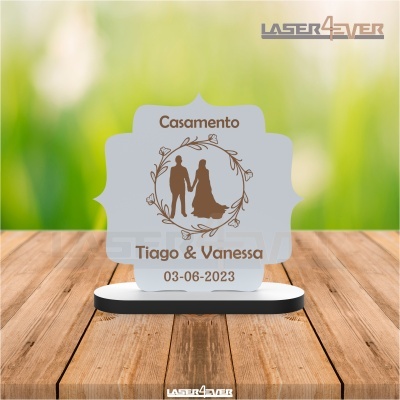 Placa decorativa de casamento com a silhueta de um casal e texto em castanho num fundo verde desfocado