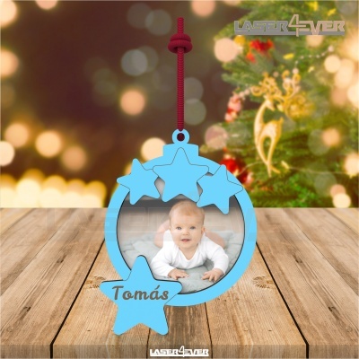 Enfeite de Natal azul com estrelas e foto de bebé, pendurado com cordão vermelho sobre madeira com fundo natalício