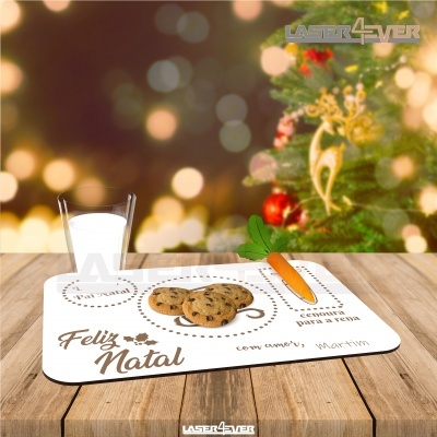 Tapete branco para ração com texto natalício, bolachas e cenoura sobre mesa de madeira junto a árvore de Natal iluminada