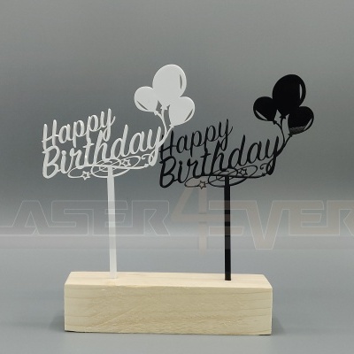 Enfeites de bolo acrílicos branco e preto com 'Happy Birthday' e balões sobre base de madeira.
