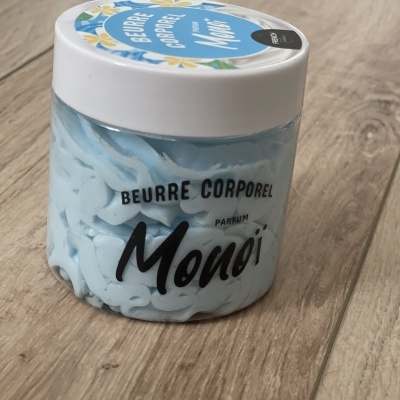 Frasco de creme corporal azul com tampa branca sobre chão de madeira clara