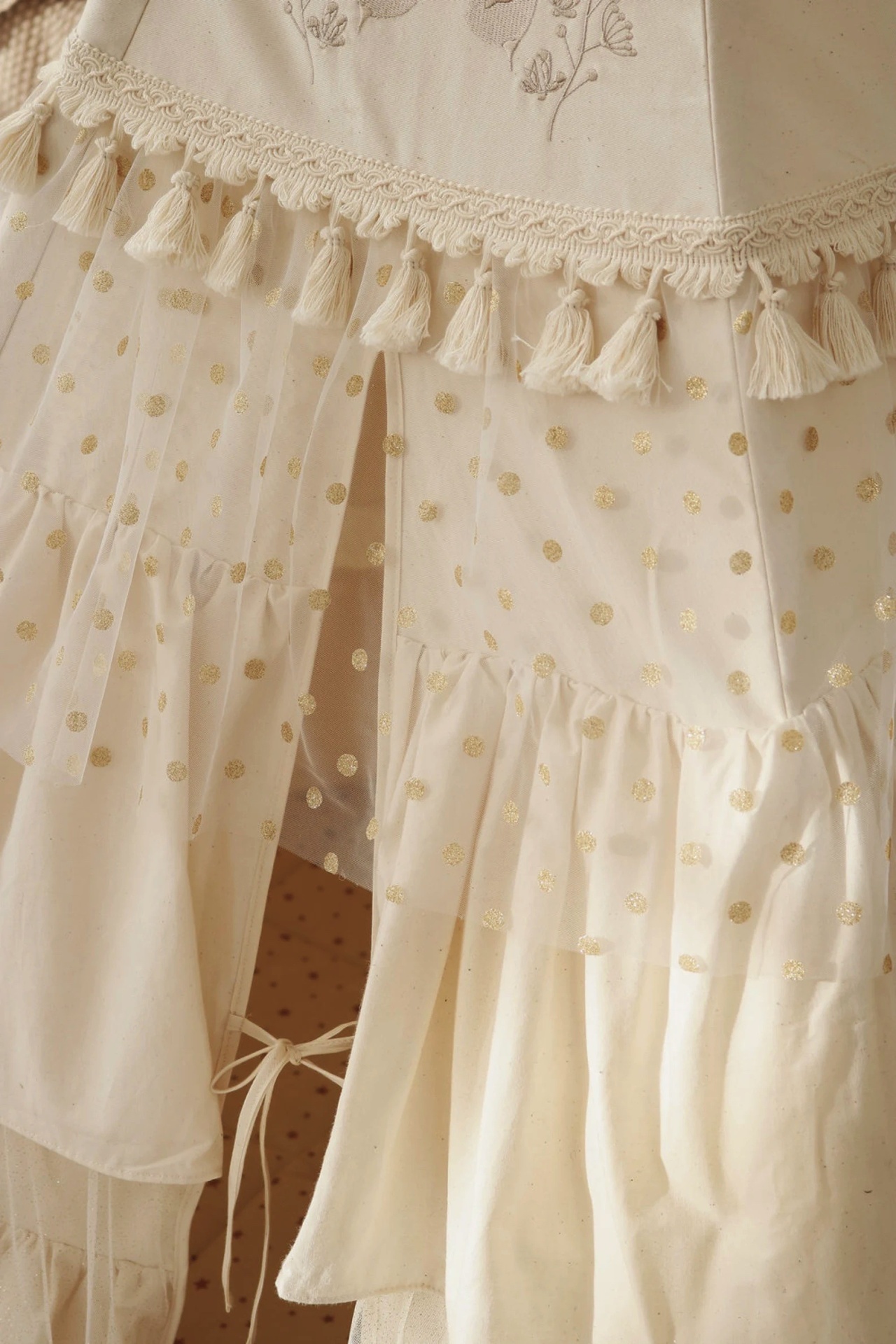 Pormenor de vestido ou saia branco com bolinhas douradas e franjas