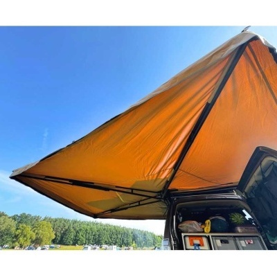 Toldo laranja anexado a veículo preto ao ar livre com céu azul e árvores