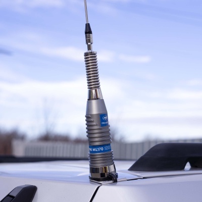 Antena metálica montada num carro branco com etiquetas azuis e céu azul ao fundo