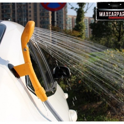 Ducha amarela a borrifar água numa janela de carro branco com edifícios ao fundo