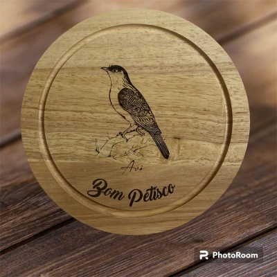 Tábua redonda de madeira clara com desenho de pássaro e texto Bom Petisco