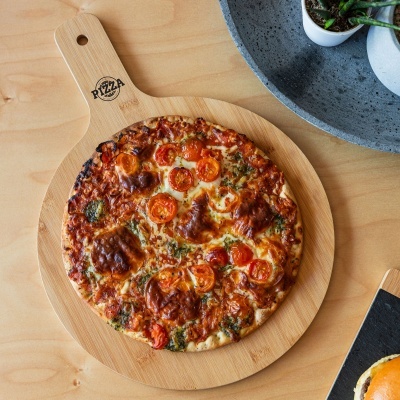 Pizza redonda com queijo e tomate cereja sobre tábua de madeira