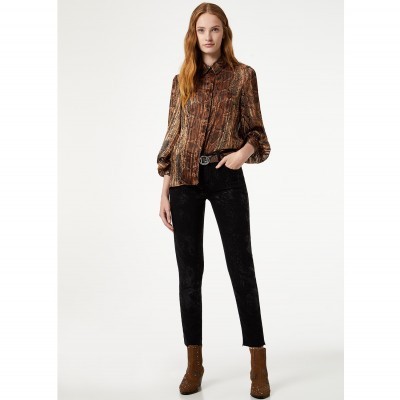 Mulher com camisa castanha estampada, calças pretas e botas castanhas.