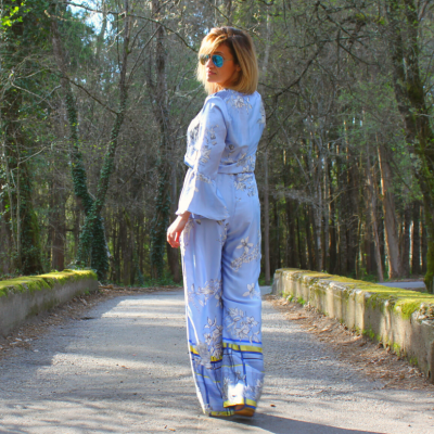 Mulher de costas usando macacão azul com padrão floral numa estrada em floresta