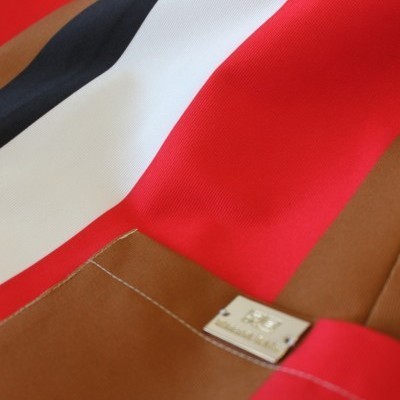 Mochila castanha com fecho metálico e faixa preta, branca e vermelha