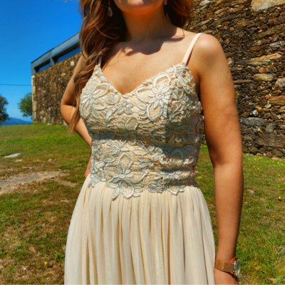 Vestido creme com corpete de renda floral e alças finas ao ar livre junto a parede de pedra
