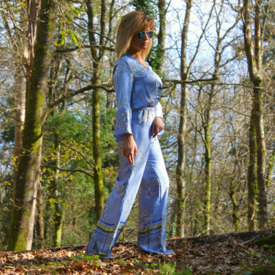 Mulher com macacão azul claro estampado, óculos escuros, em floresta