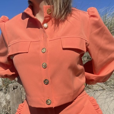 Blusa laranja de mulher com botões dourados e bolsos no peito na praia
